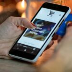 Woman using smartphone for online shopping with credit card in hand, festive background lighting.