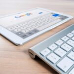 A modern tablet displaying a search engine logo next to a wireless keyboard on a wooden desk.